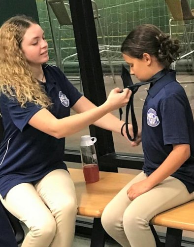 A woman is helping another girl with her necklace.