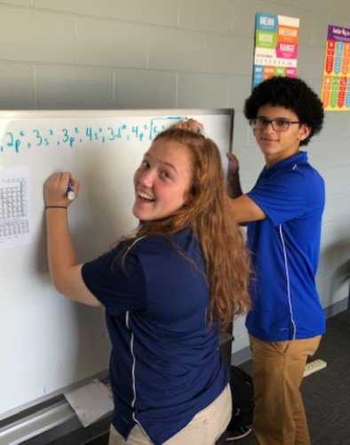 Two people are writing on a whiteboard.