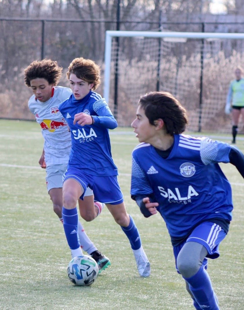 Three young men playing soccer on a field.