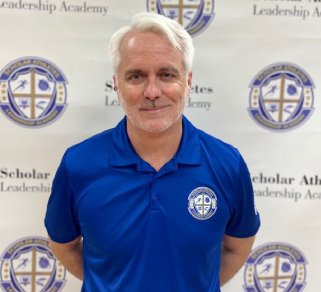 A man in blue shirt standing next to a white wall.