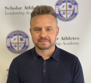 A man in front of a school logo.